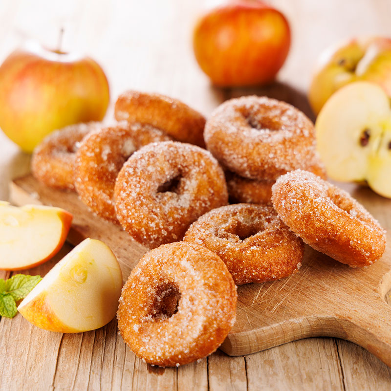 Apple cinnamon donuts dusted with sugar and surrounded by sliced apples