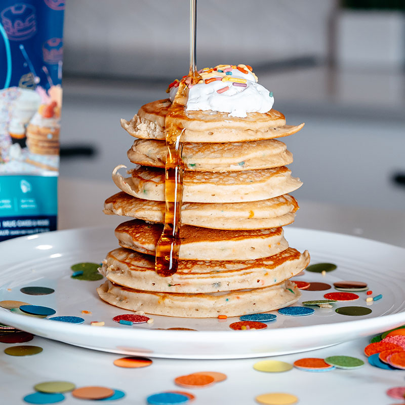 Stack of vanilla confetti pancakes with whipped cream, sprinkles and syrup
